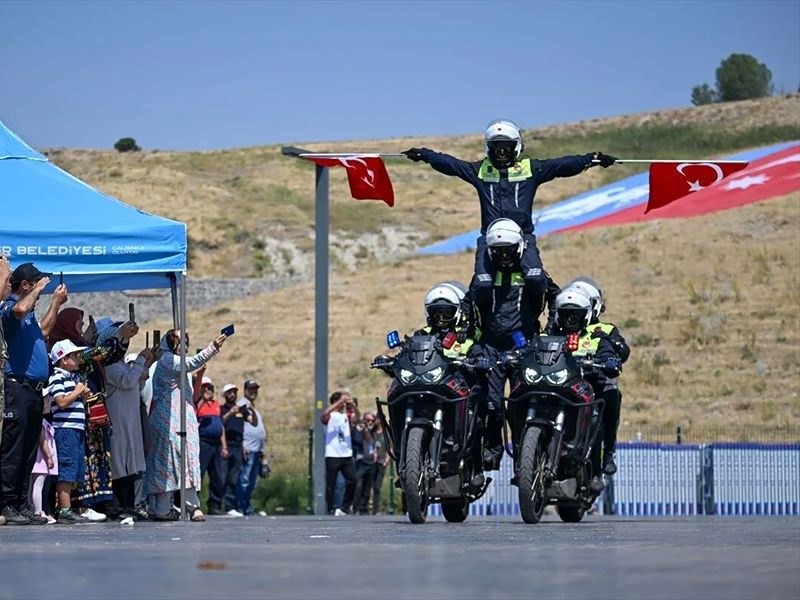 Motosikletin üzerinde ayakta duran polis, kollarını iki yana açmış hâlde gösteri yapıyor