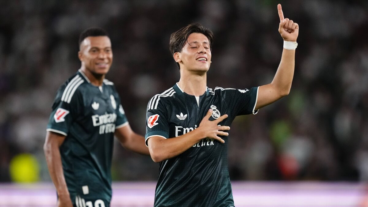 1200x675. Arda Güler Real Madrid deplasman formasıyla gol sevinci, parmağı gökyüzünde, elini göğsüne koymuş; solda Mbappé gülümsüyor. Temiz, yazısız.