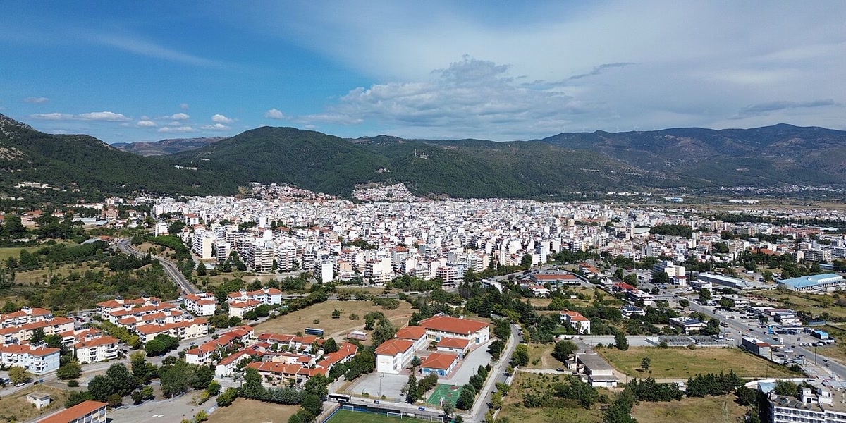 İskeçe (Xanthi) şehrinin havadan geniş görünümü: yerleşim, arkada dağlar ve bulutlu mavi gökyüzü; Batı Trakya bölgesini anlatan temiz kare (1280x641, CC0)