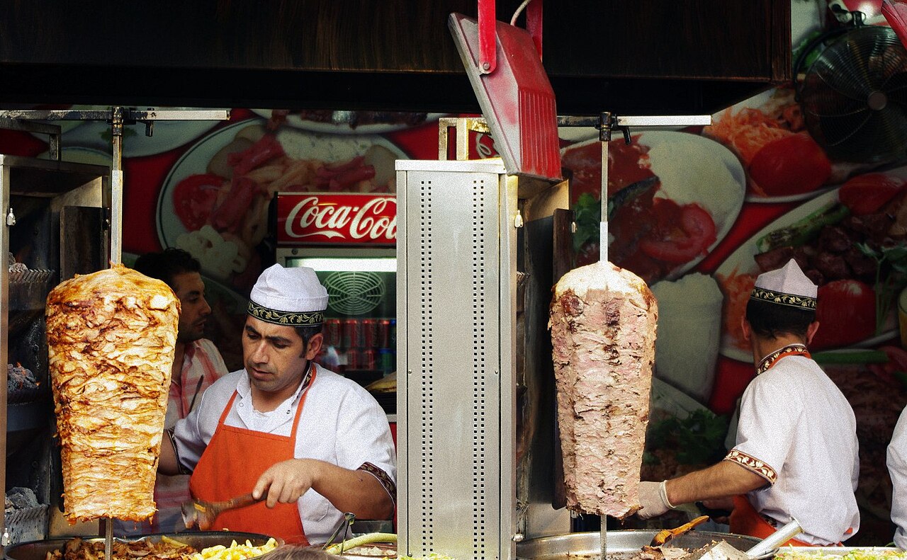 GÖVDE — İstanbul'da iki döner şişi ve dönerci ustalar (arka planda küçük Coca-Cola tabelası var). Wikimedia Commons, CC