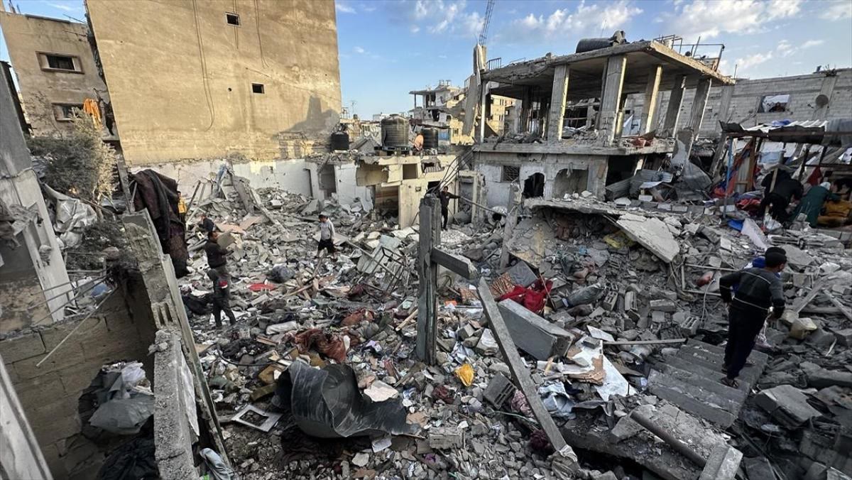 GÖVDE FOTOĞRAFI — Gazze'de yıkılmış bir bina enkazı üzerinde arama yapan siviller; moloz yığınları arasında birkaç kişi eşya/kalıntı topluyor. Gündüz, net, yatay.