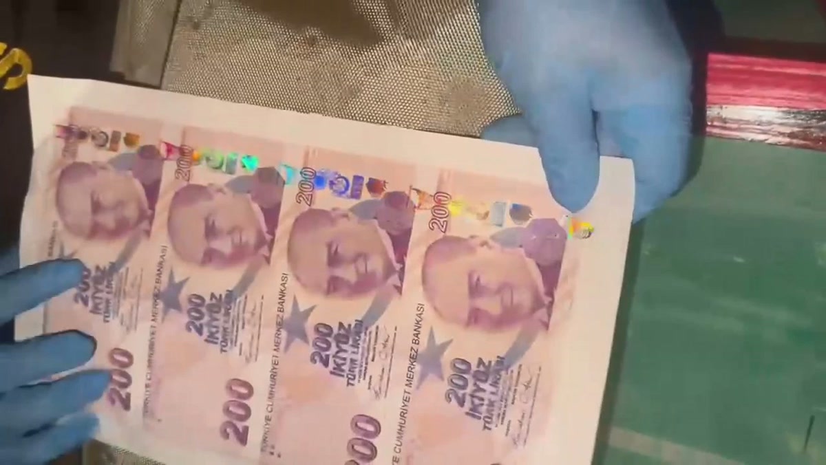 1280x720, eldivenli polisin elinde 4'lü kesilmemiş sahte 200 TL tabakası, arkada yeşil baskı tezgâhı. Net, logosuz; gövde fotosu için ideal.