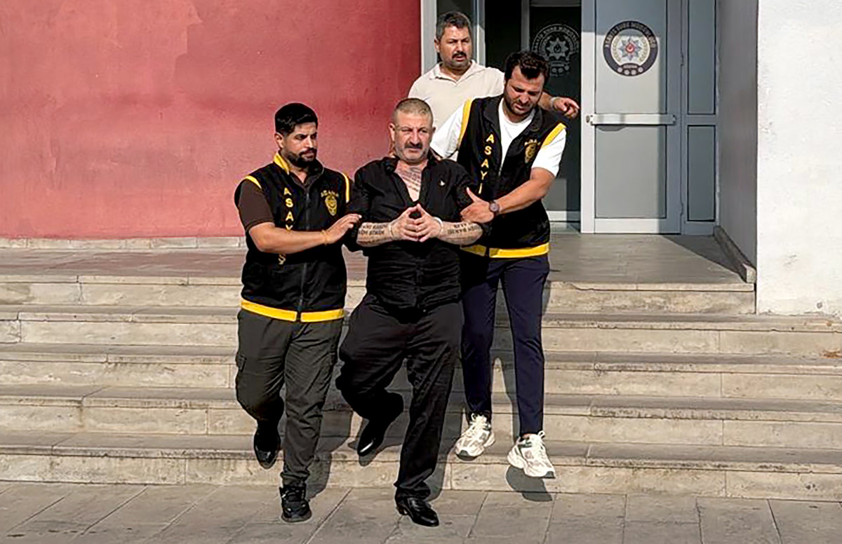KAPAK ÖNERİSİ (2047x1323): Şükrü Akçay, yelekli Adana Asayiş polisleri arasında emniyet binasının merdivenlerinden indirilirken; tek kare, net, yazısız, kolaj değil
