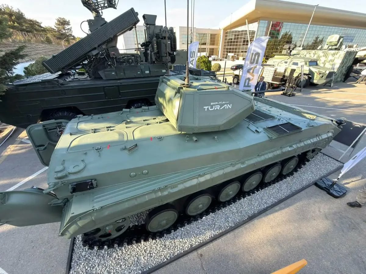KAPAK ÖNERİSİ: BMP-1TA TURAN, Bakü ADEX 2026 açık hava sergi alanında çakıl zemin üzerinde; kulesinde 'BMP-1TA TURAN' yazısı net, arka kapakları açık, arkada fuar binası ve başka araçlar. 1200x900, temiz, filigransız.