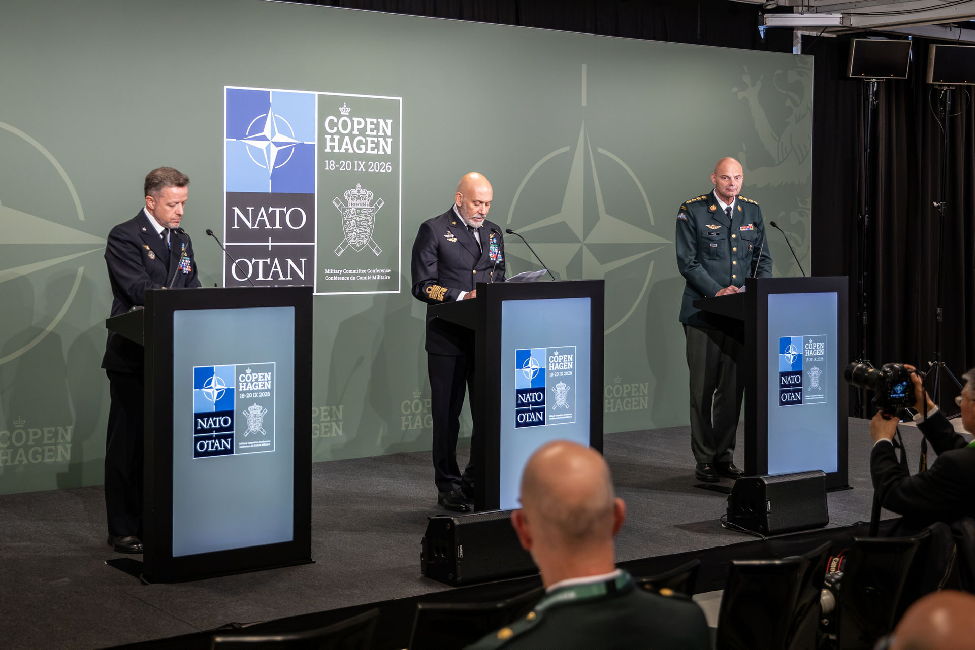 Basın toplantısı geniş plan: üç kürsü, Cavo Dragone konuşurken, sağda Hyldgaard; NATO resmi fotoğrafı