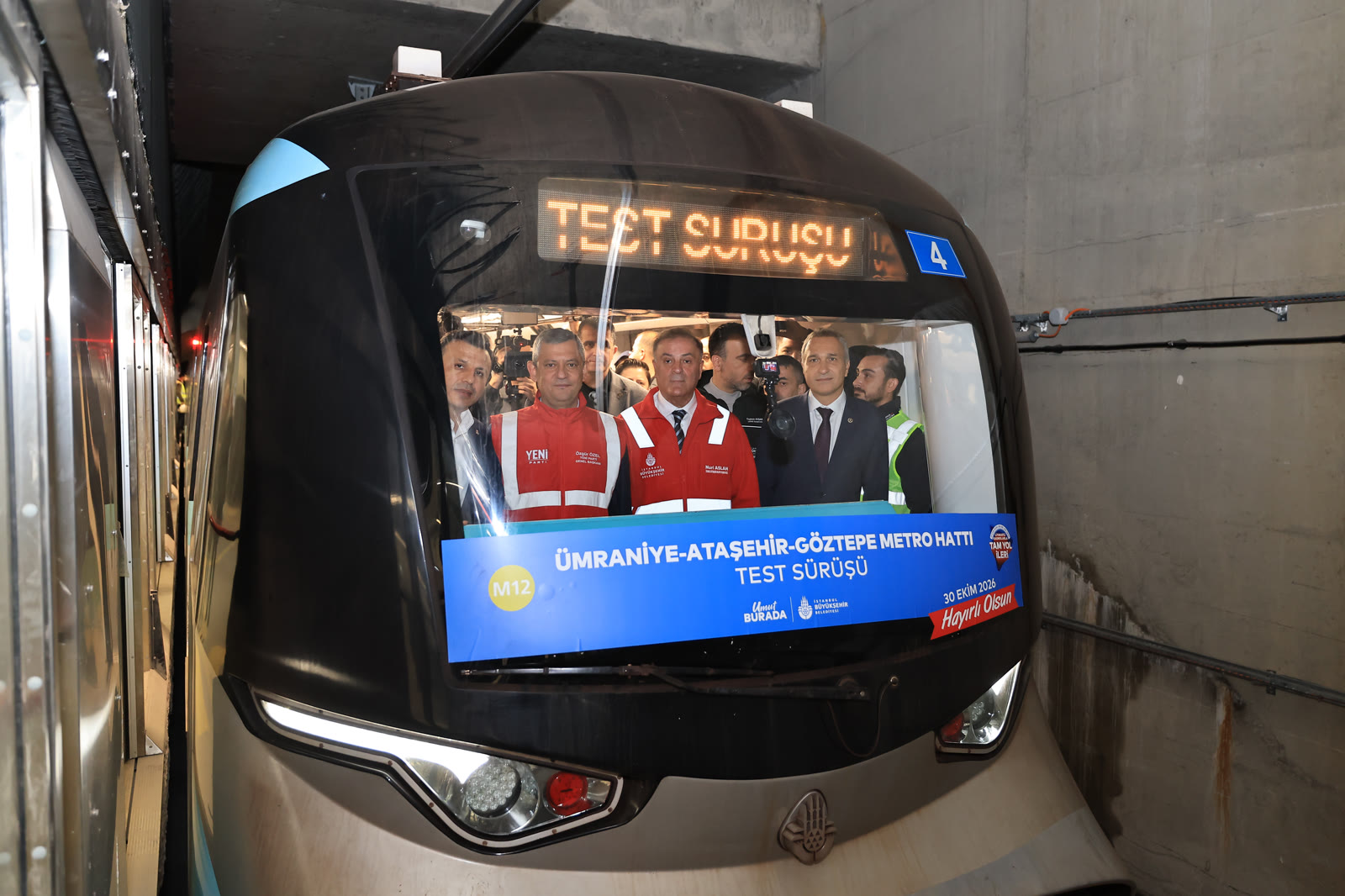 Test sürüşü için hazırlanan metronun ön camında Özgür Özel (solda, Yeni Parti yeleğiyle) ve Nuri Aslan (İBB montuyla)