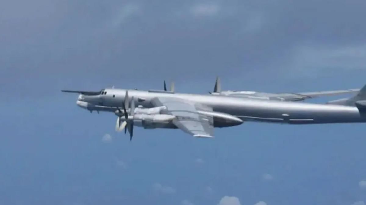 Tu-95 havada yandan görünüş, bulutlu mavi gökyüzü; video karesi olduğundan hafif yumuşak ama temiz ve yazısız, 1200x674