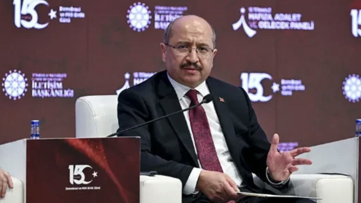 Salih Tanrıkulu bir panelde mikrofon önünde, beyaz koltukta oturuyor; arka planda İletişim Başkanlığı etkinlik panosu. 1280x720, net, filigransız yakın plan.