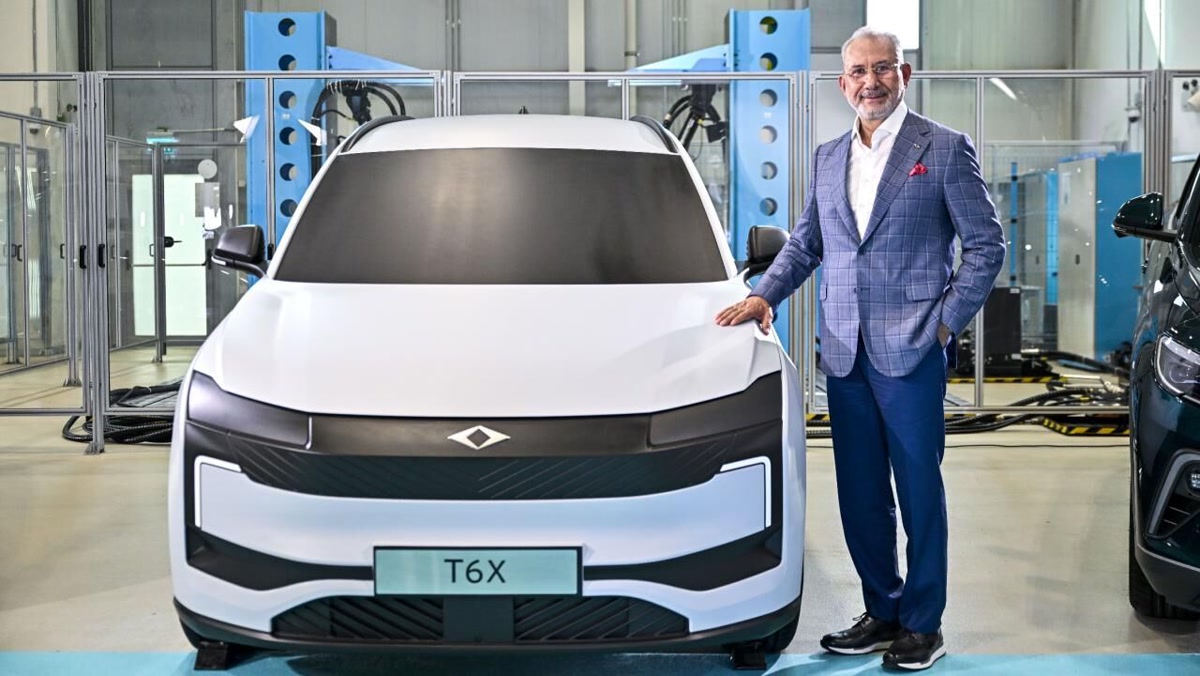 Togg Yönetim Kurulu Başkanı Fuat Tosyalı, T6X prototipinin yanında ayakta poz veriyor; tesis içi, temiz kare, 1280x720. Gövdeye ya da ikinci kapak adayı.