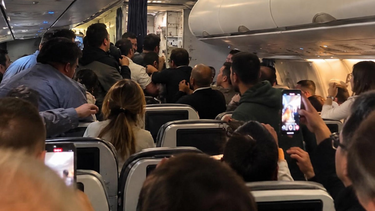 Uçak kabininde ayakta bekleyen, telefonla çeken yolcular; 1280x720, temsili kabin karesi (olayın kendisi olduğu teyit edilmedi).